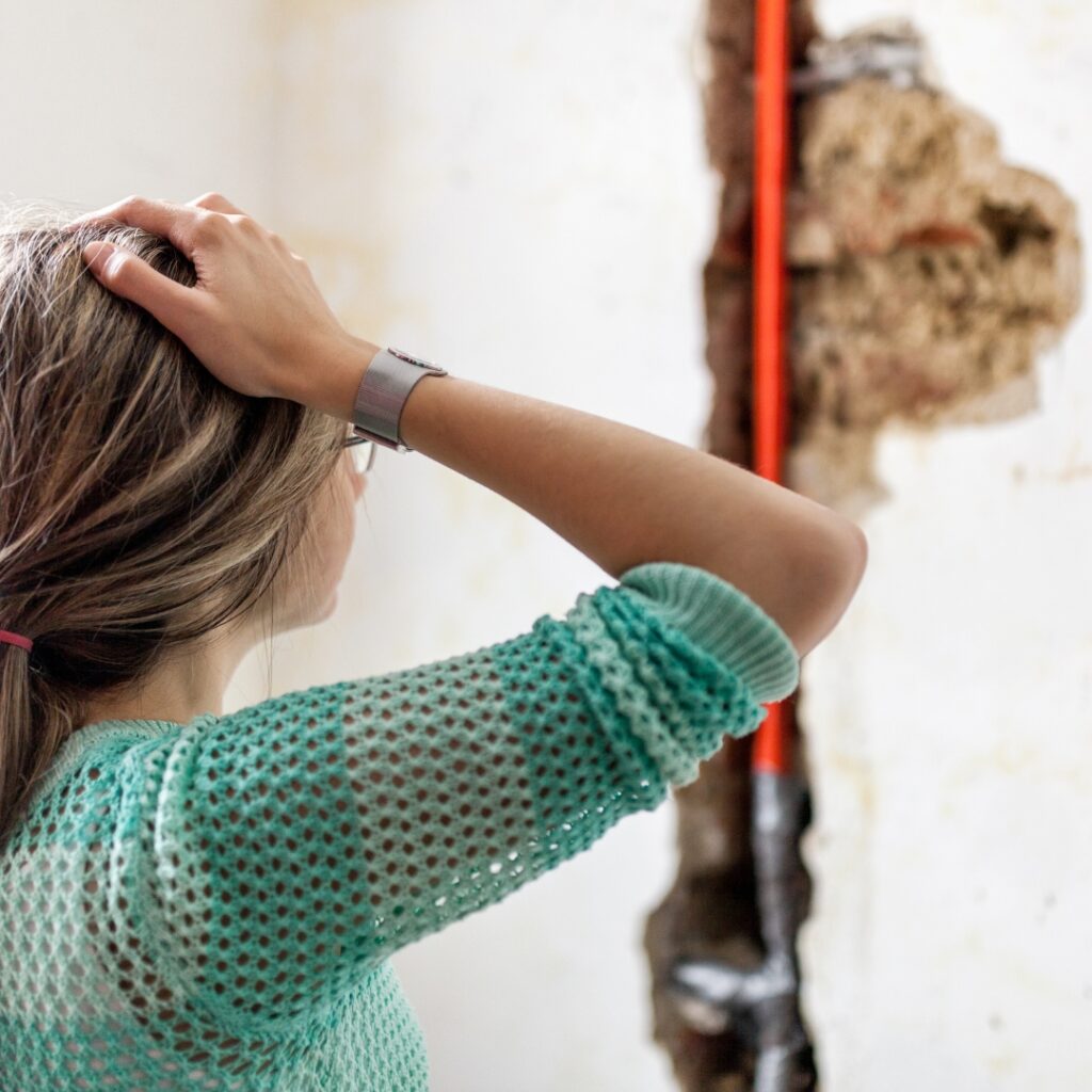 woman looking at wall damage from leaking pipe